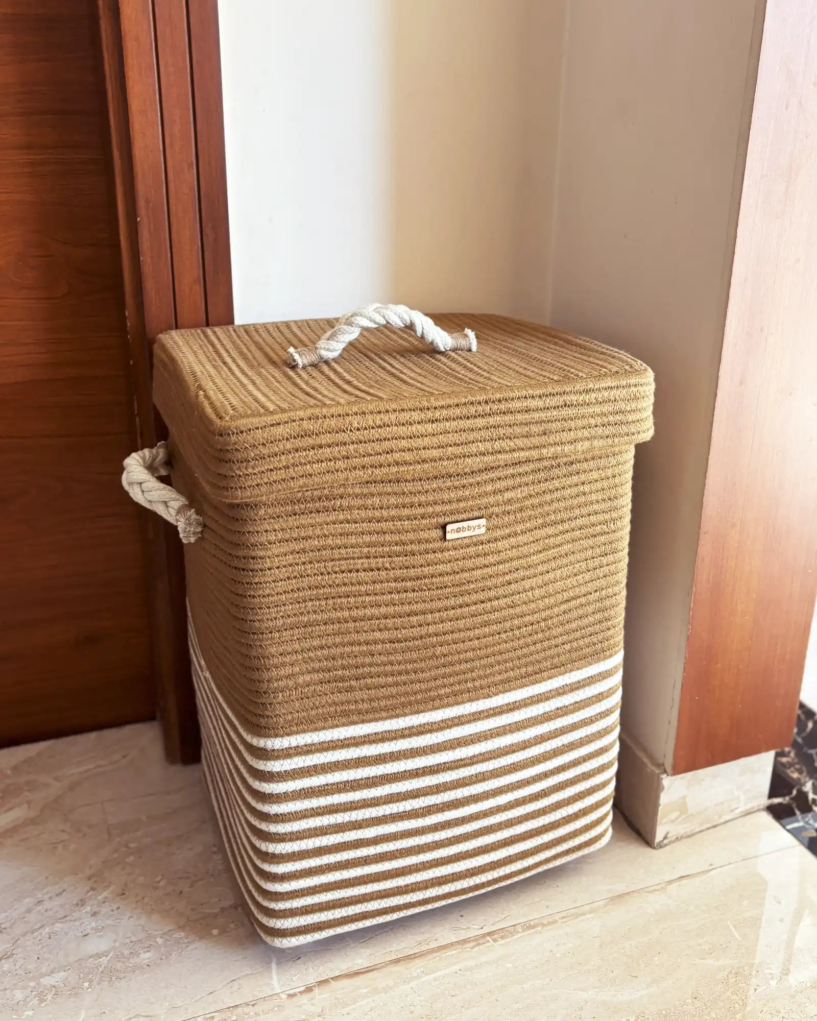 Brown and beige striped laundry basket with a handle on a wooden floor